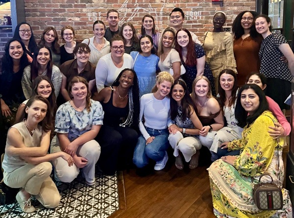 Group photo of about 25 people together in front of a brick wall.